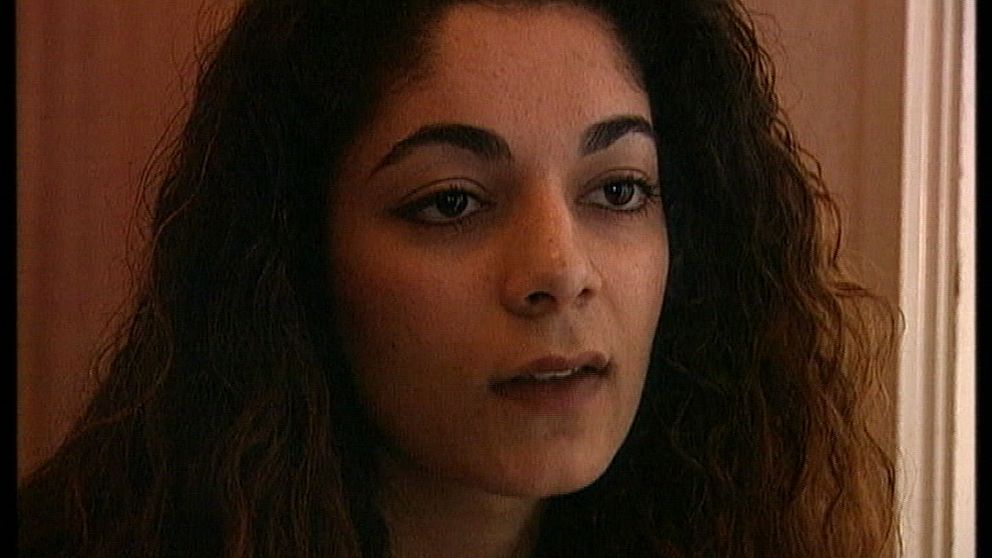 En kvinna med mörka ögon och tjockt mörkt lockigt hår tittat ut ur bild.