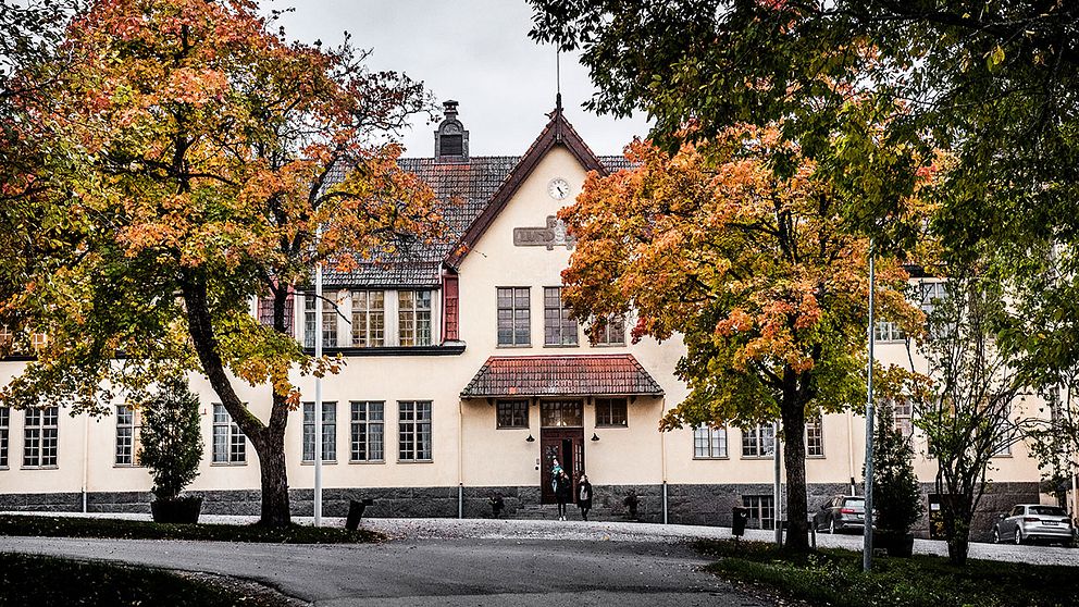 En vy av en skolbyggnad med höstfärger, omgiven av färgglada träd i rött och gult.