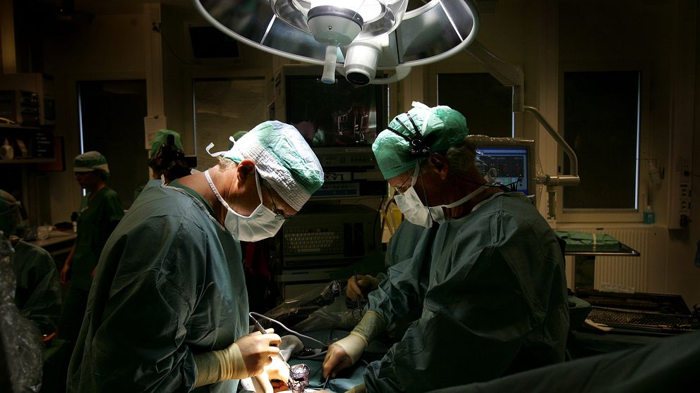 Två personer i operationskläder står över ett operationsbord med patient