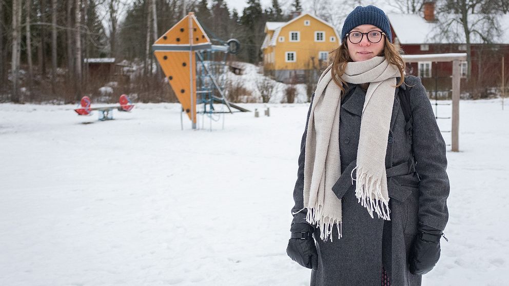 Ett porträtt på Isabelle Axellson, det är några centimeter snö ute och Isabelle står på en lekpark med en gul klätterställning i bakgrunden.