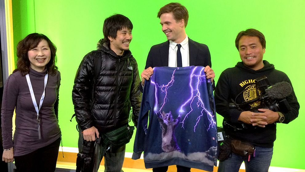 Översättaren Takako Makino (t.v.) tillsammans med SVT:s meteorolog Nils Holmqvist och hans världskända tröja. Reportern Shohei Umemura och fotografen Mutsuaki Kiyohara från TV Tokyo tog sig till SVT-huset just på grund av den klassiska kattröjan.