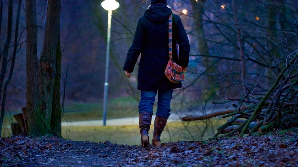Ensam höstklädd kvinna går på stig genom mörk park
