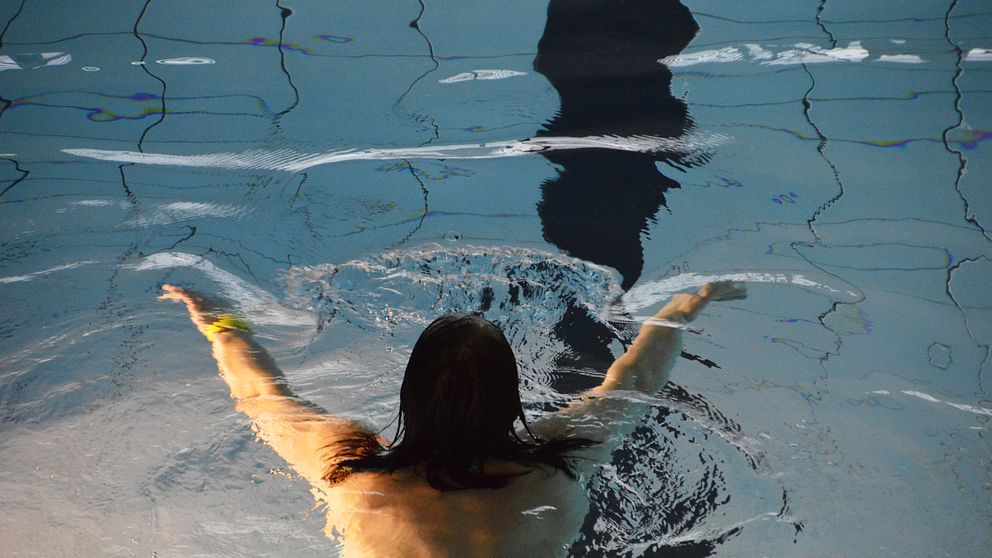 Kvinna sedd uppifrån simmar i en bassäng.