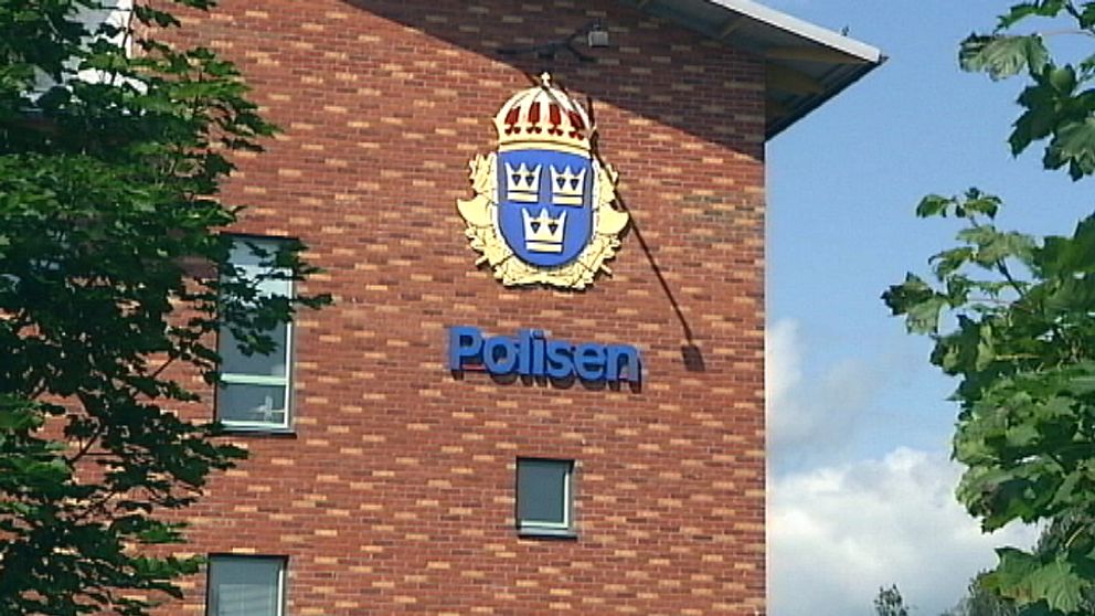 Polishuset i Karlstad med löv i förgrunden, emblem på fasaden, sommartid