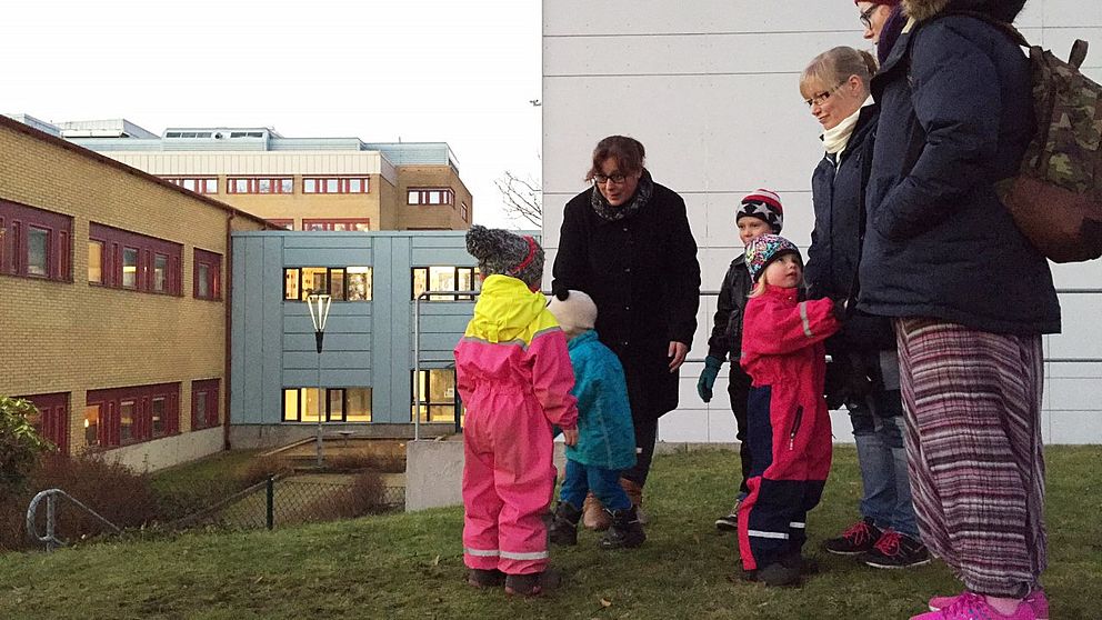 Tre vuxna och fyra barn står tillsammans utanför en vit byggnad.