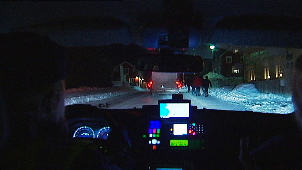 Bild inifrån polisbil ut på snöig väg med trafik och människor.