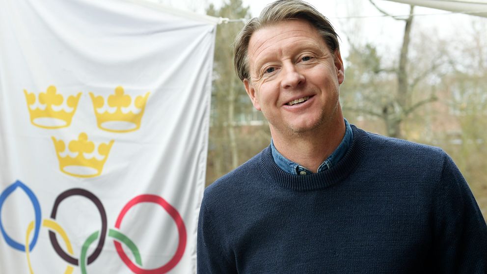 Hans Vestberg står bredvid en flagga med de olympiska spelens ringar.