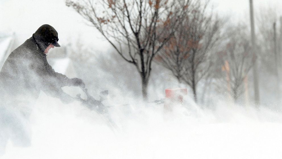 man med snöslunga i blåsigt vinterväder