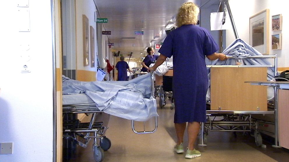 En sjuksköterska flyttar två sängar med patienter i en sjukhuskorridor.