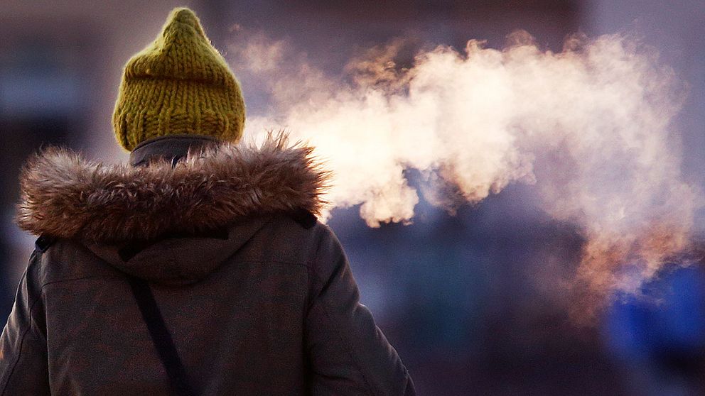 Kallt ute, kvinna med yllemössa bakifrån som andas ut rök i kylan