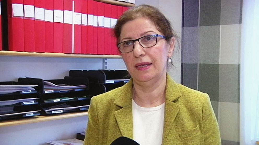 Kvinna med mörkt uppsatt hår och glasögon står i sitt kontor.