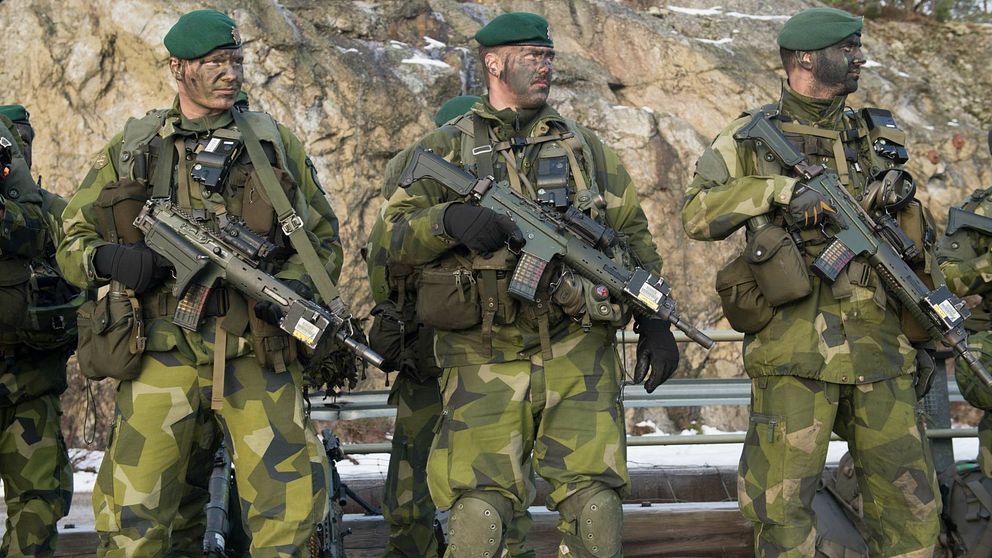 Tre beväpnade militärer med kamoflagemålning i ansiktet