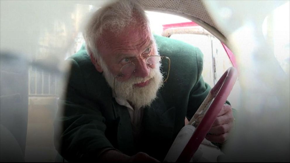 Äldre man böjer sig in i en bil.