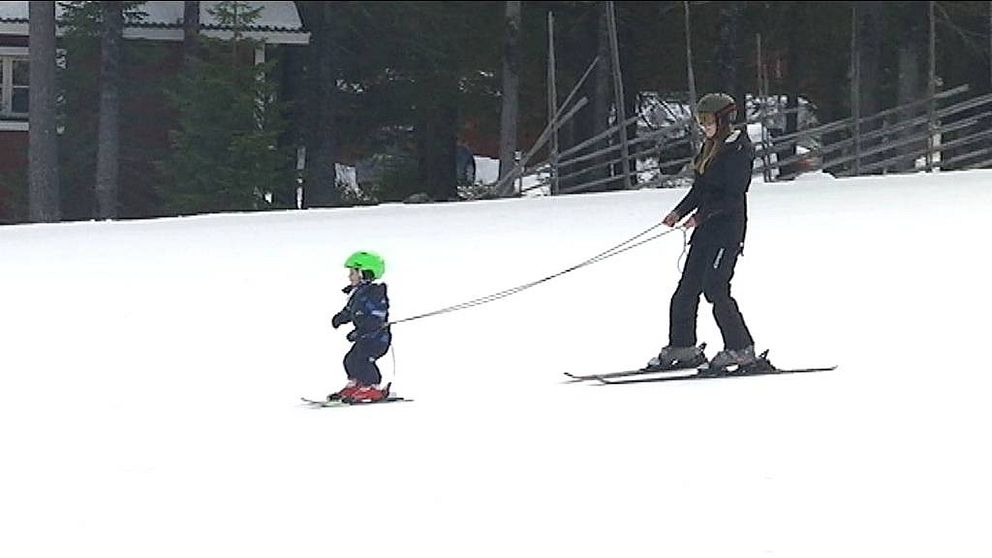 Kvinnan på skidor bromsar ett litet barn som hålls i remma