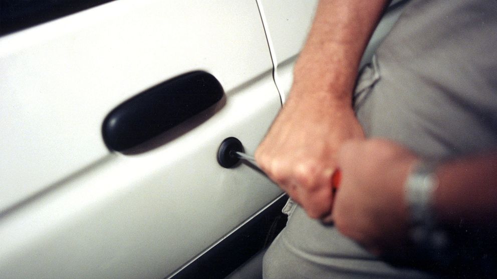 En person gör inbrott i en bil med en skruvmejsel