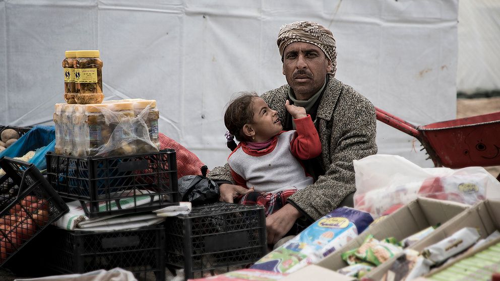 Muhammed och hans dotter Adiva har bott några veckor i flyktinglägret utanför Mosul. De säljer frukt och grönsaker och försöker få vardagen att någorlunda normal i väntan på att kunna återvända hem till Mosul.
