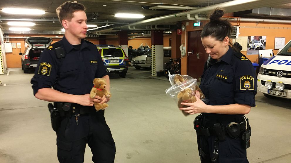 Två poliser står i ett garage. Har nallebjörnar i händerna.