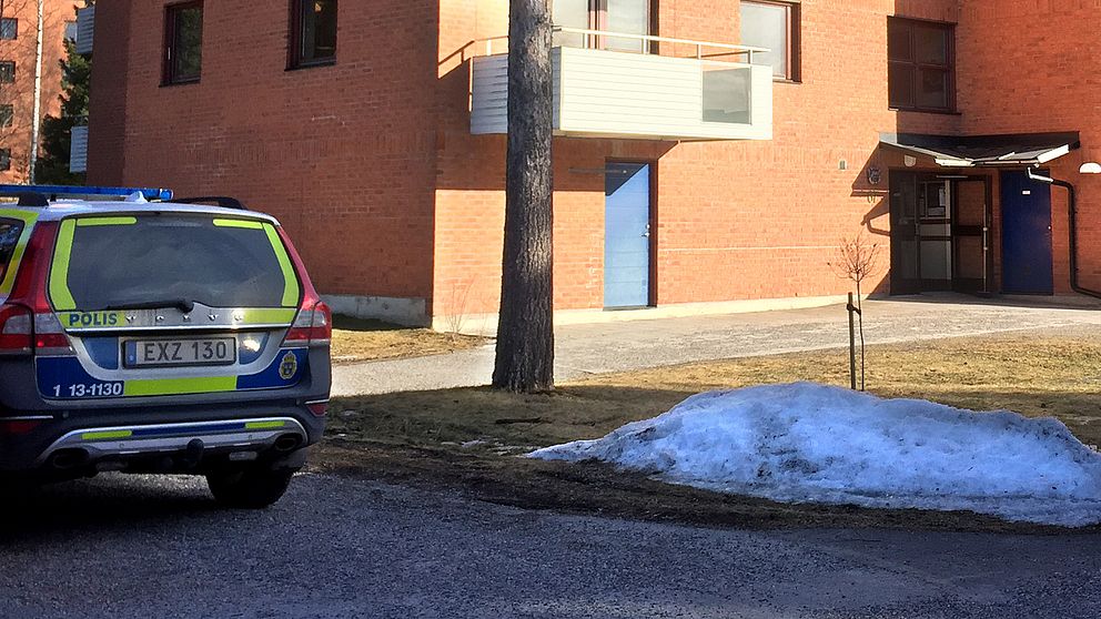En polisbil står parkerad utanför ett hus av tegel.
