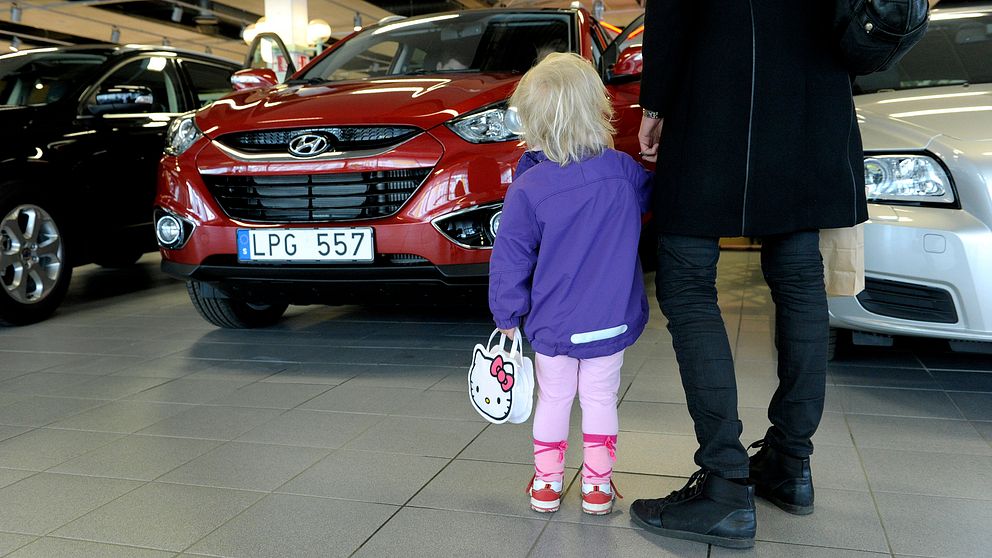 En kvinna kollar på en bil med ett barn.