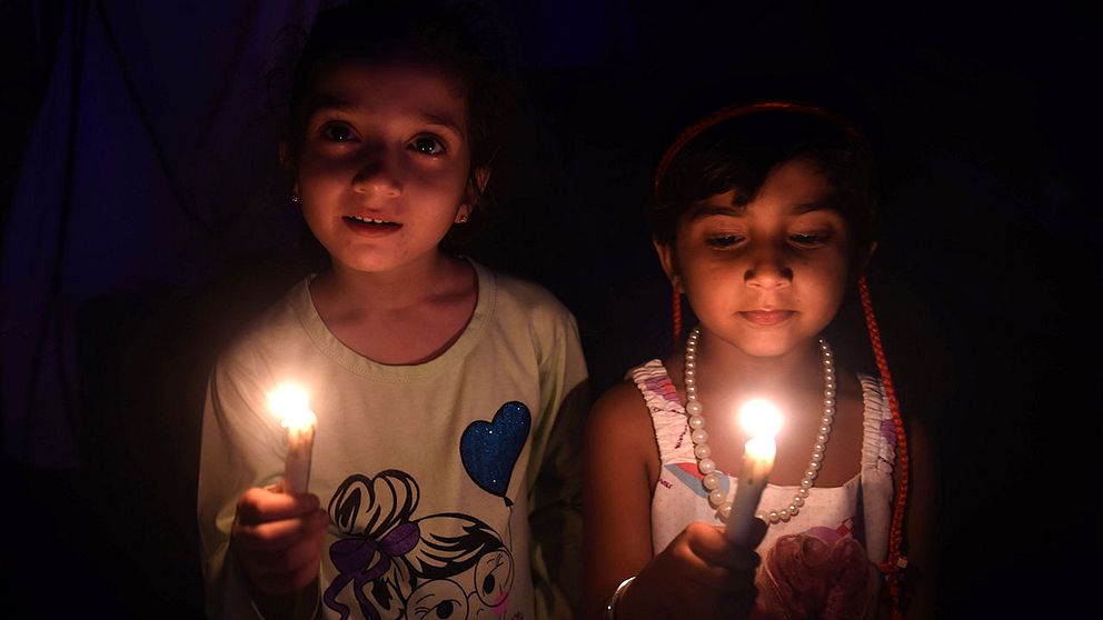 Två flickor i Karachi, Pakistan, tänder ljus när lamporna släckts.