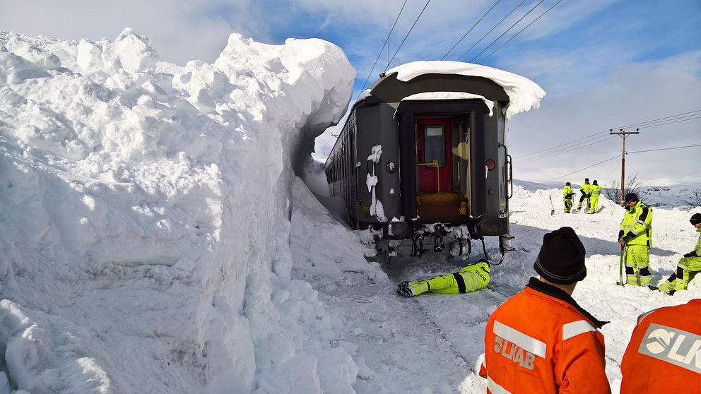 Ett tåg som fastnat längs malmbanan och en jättestor snövägg som stoppar tåget.