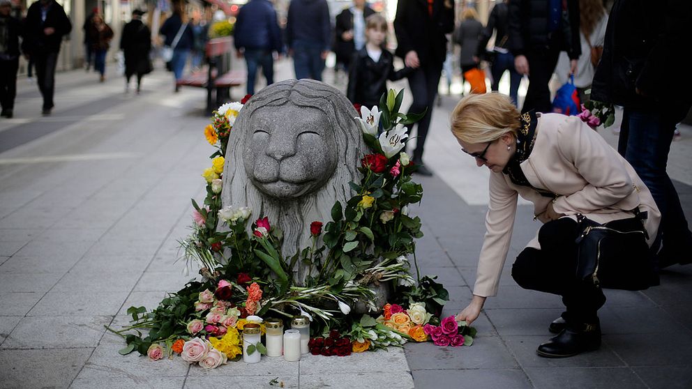 En kvinna lägger ned blommor vid ett betonglejon på Drottninggatan.