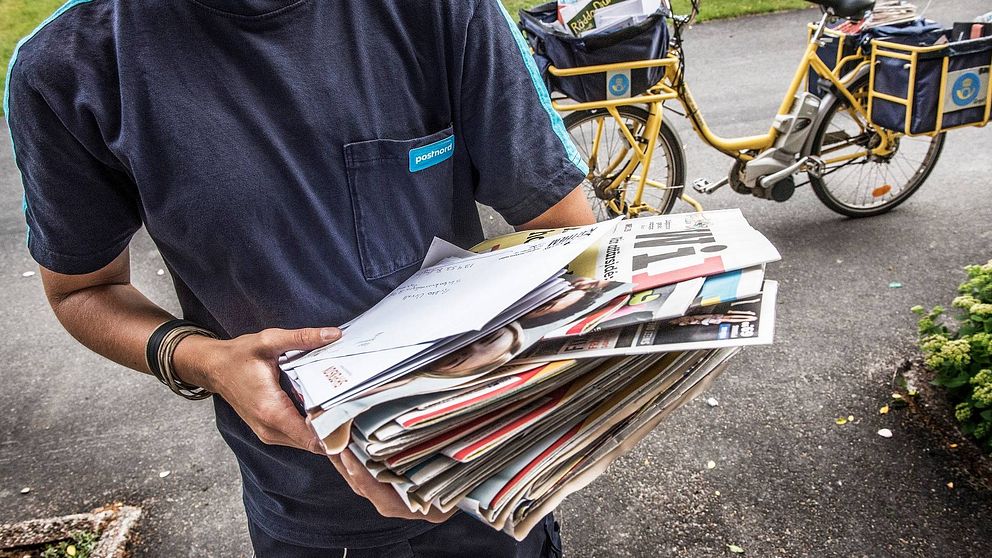 Brevbärare håller post i famnen, i bakgrunden en postcykel.