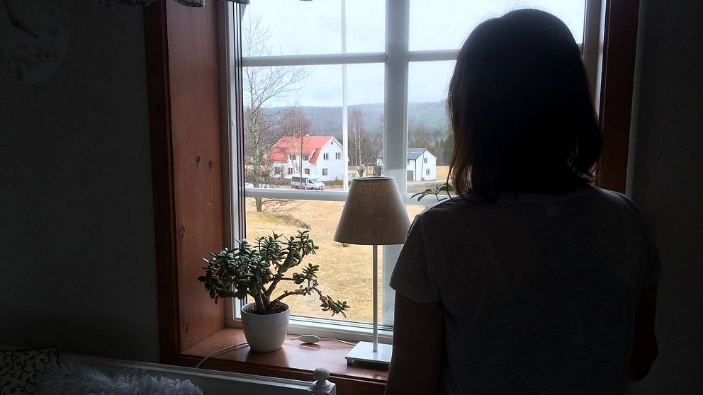 Ung kvinna står och tittar ut genom fönster.