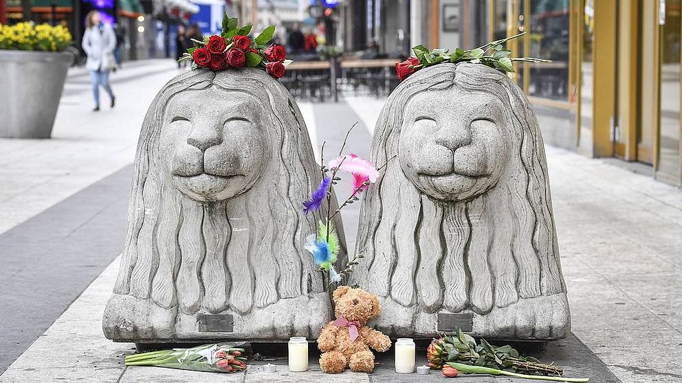 Två betonglejon på Drottninggatan, de har rosor på huvudena och blommor framför sig