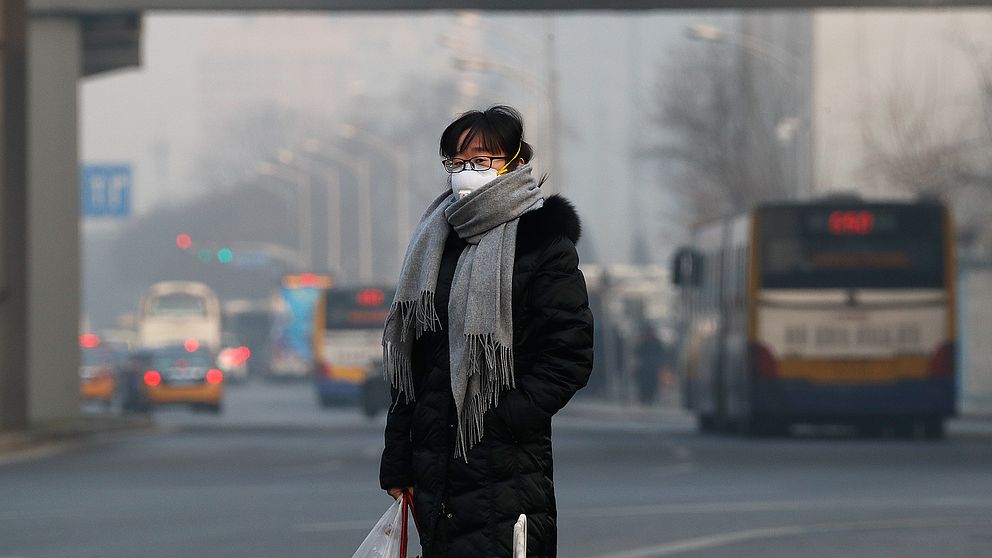 En kvinna i andningsmask står på en gata i Peking, Kina.