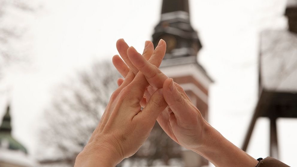 Händer som tecknar ”kyrka” framför domkyrkan i Västerås.