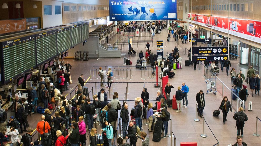 Avgångshallen på Arlanda sedd uppfrån. Folk rör sig i hallen, andra checkar in. Till vänster tavlor med avgångstiderna