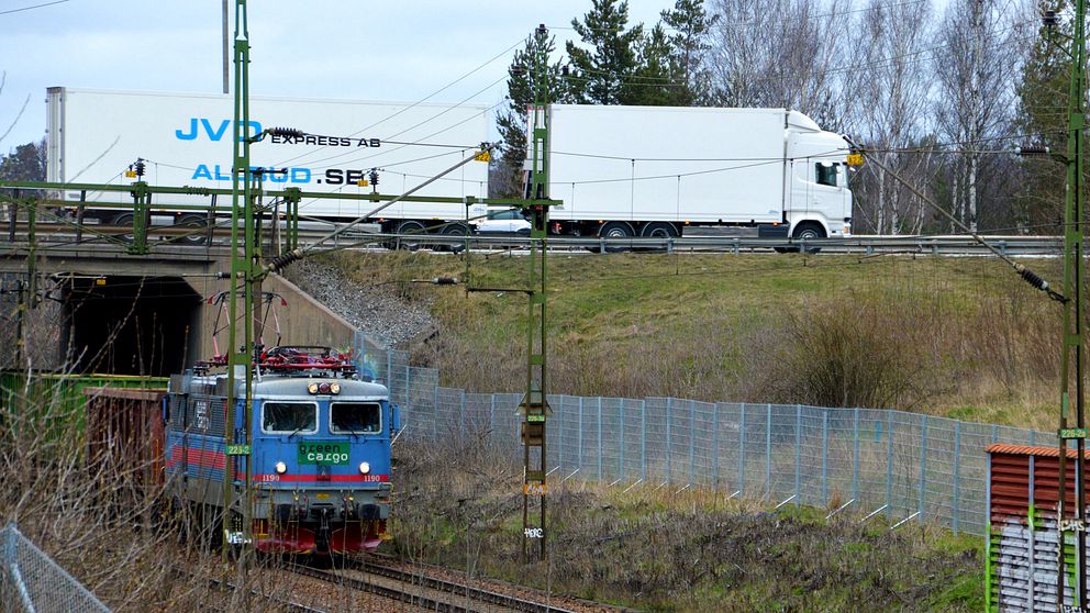 Ett tåg passerar i en tunnel under en väg. Ovanför färdas en lastbil.