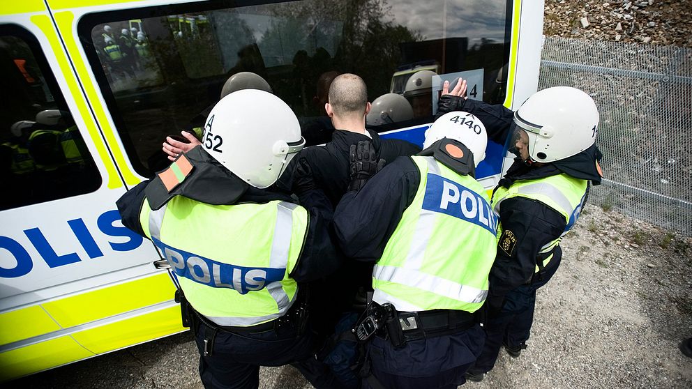 Tre poliser håller fast en demonstrant mot en polisbuss.
