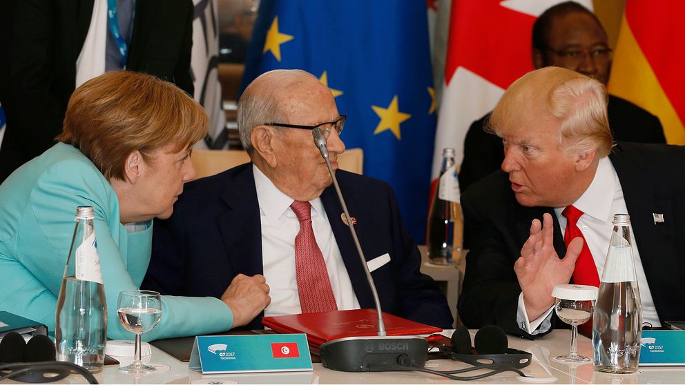 Tysklands förbundskansler Angela Merkel i turkos dräkt för livliga diskussioner med USA:s president Donald Trump i röd slips. Tunisiens president sitter mellan dem och följer samtalet.