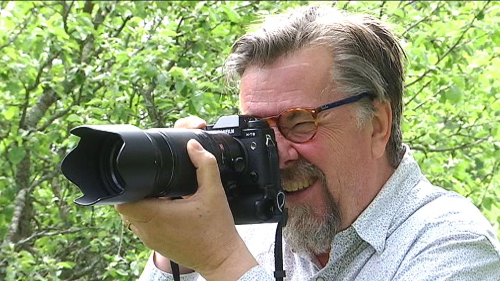 Fotografen Lars Dahlström står i prickig skjorta och tittar in i en kamera.