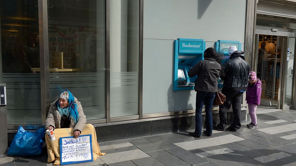 En kvinna tigger utanför en bank i Stockholm.