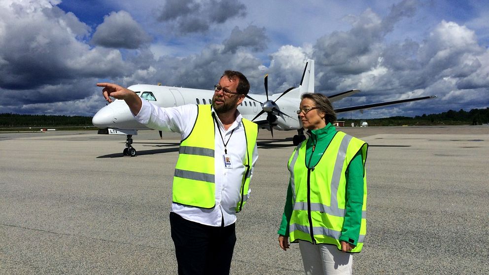 Mikael Smedberg och Helena Vilhelmsson i gula reflexvästar står på flygplatsen och diskuterar