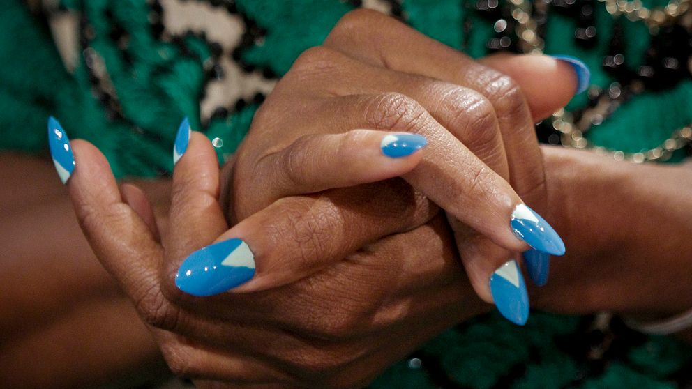 Kvinnas händer med naglar målade i blå och vit färg.