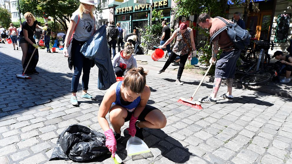 En kvinna sitter på knä med en lite sop i händerna och gör rent på kullerstensgatan.