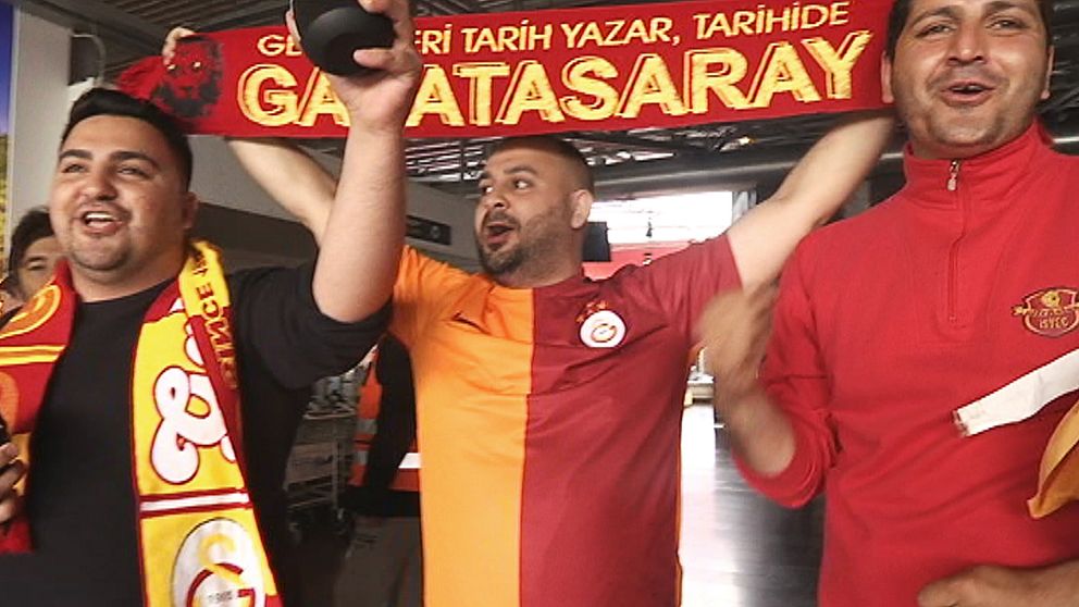 tre sjungande, glada turkiska män i klubbtröjor och med banderoll