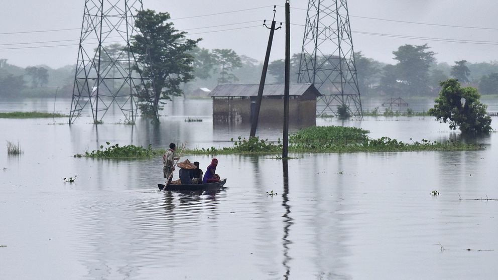 Människor reser med båt genom en översvämmad by nära nationalparken Kaziranga.