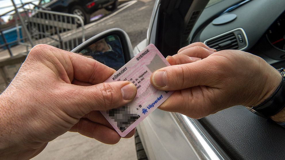 Två händer som håller i ett körkort som sträcks ut genom en bilruta