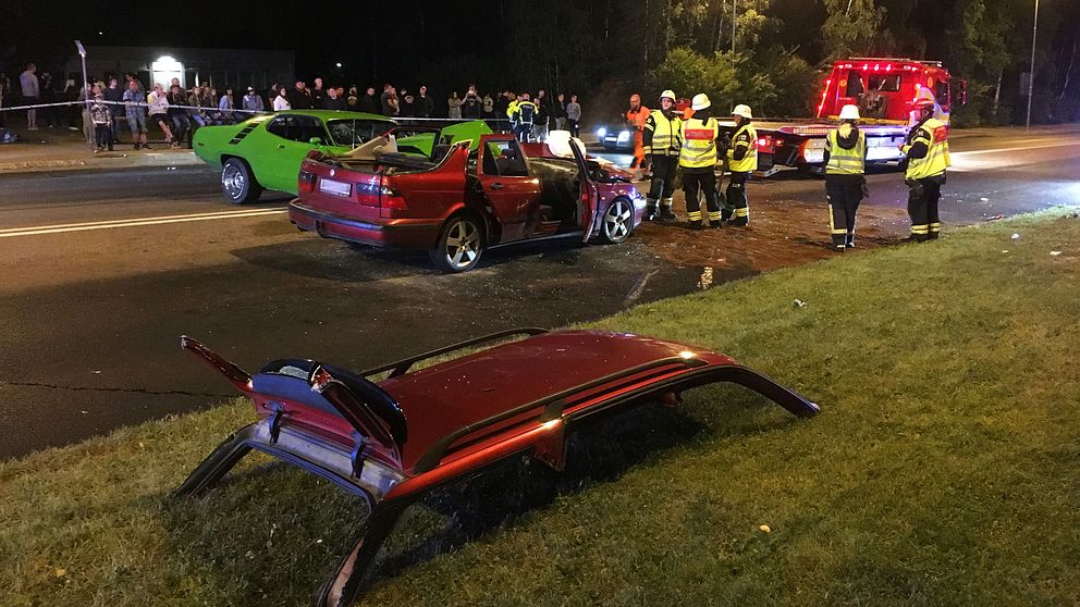 En grön bil har kört in i en röd bil. Den röda bilen är helt förstörd, taket är av och ligger på marken.