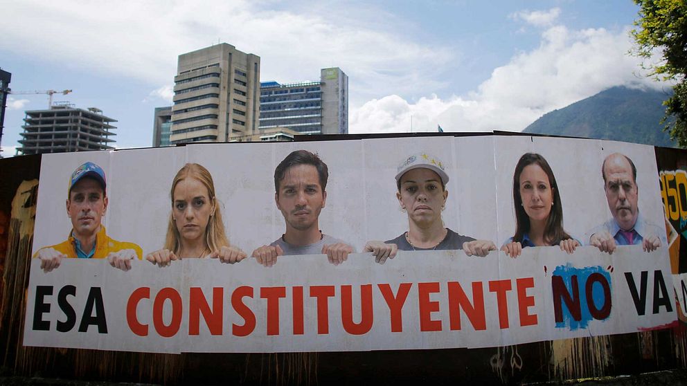 Bild på affisch på ett plan framför några höghus. På affischen ses sex oppositonsledare med en skylt där det står ”Esa constituyente no va”.