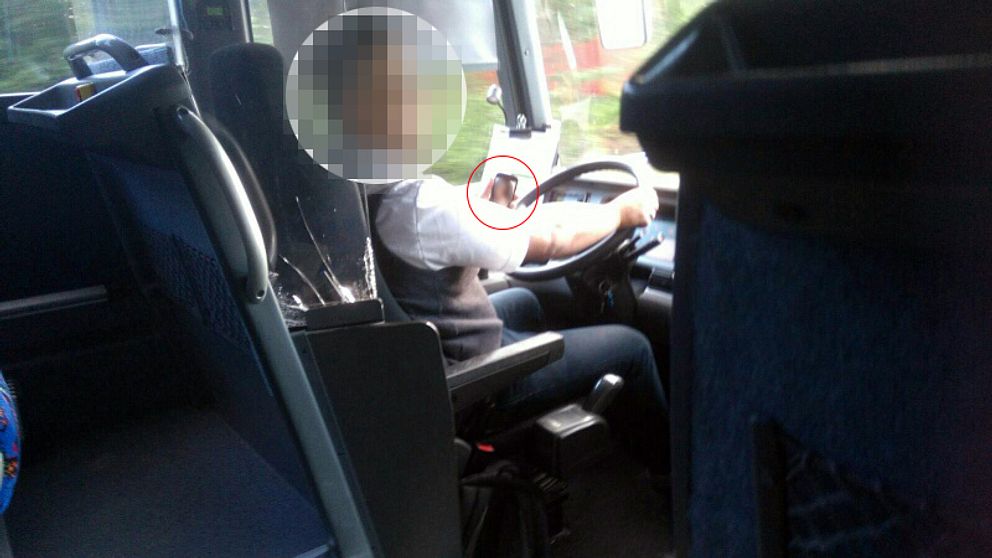 En busschaufför kör buss och håller mobiltelefonen i vänstra handen.