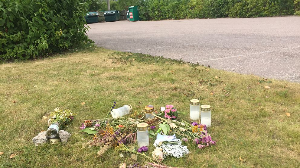 Här, på gräsmattan, intill mordplatsen har flera personer lagt ljus och blommor för att hedra den mördade kvinnan.