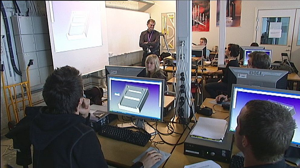 Studenter vid dataskärmar, lärare i bakgrund.