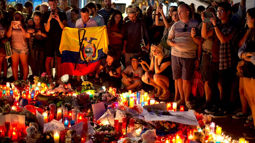 Människor samlas kring en minnesplats fylld av ljus och blommor i Barcelona