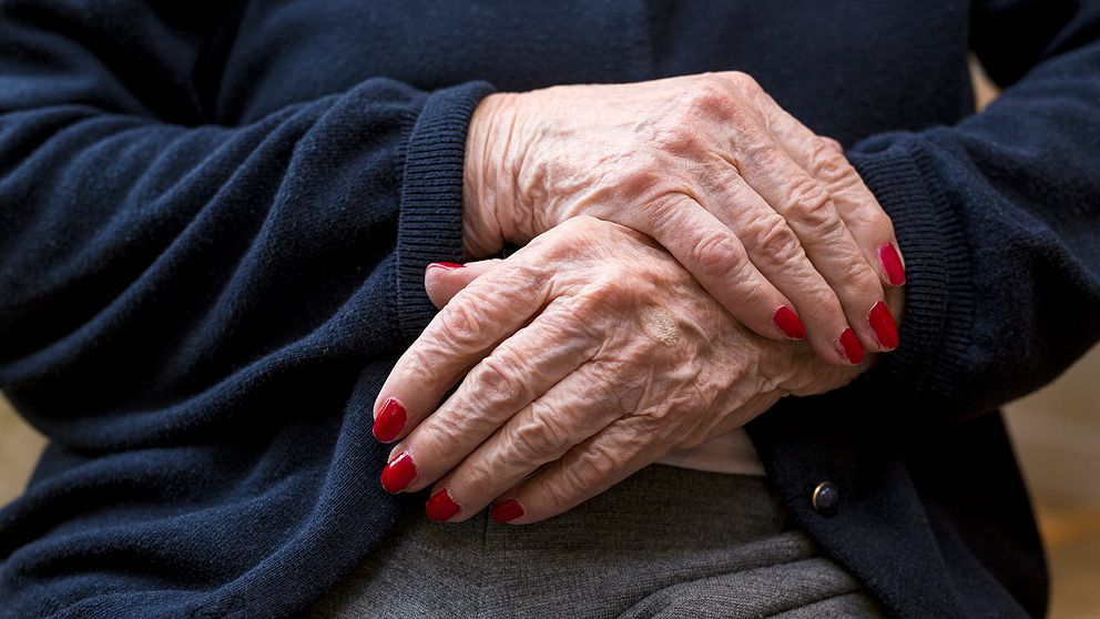Äldre kvinnas händer med rött nagellack.